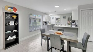 Una cocina moderna con armarios blancos, una mesa de comedor con cuatro sillas y un estante negro con objetos decorativos.