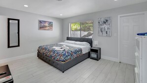 Un dormitorio moderno con una cama grande, una mesita de noche y una puerta. Tiene una ventana con persianas.