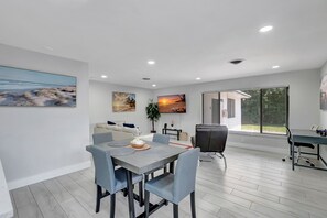 A modern living room with a dining area, a sofa, a coffee table, and a TV mounted on the wall. - Gorgeous spacious  2bd 2bath sleeps 6 private yard, parking, gas grill, dogs ok (Delray Beach)