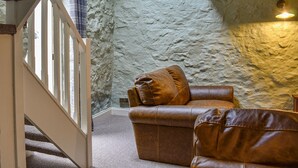 Ein Zimmer mit einer Steinwand, einem braunen Ledersofa und einer Treppe mit einer weißen Geländer.