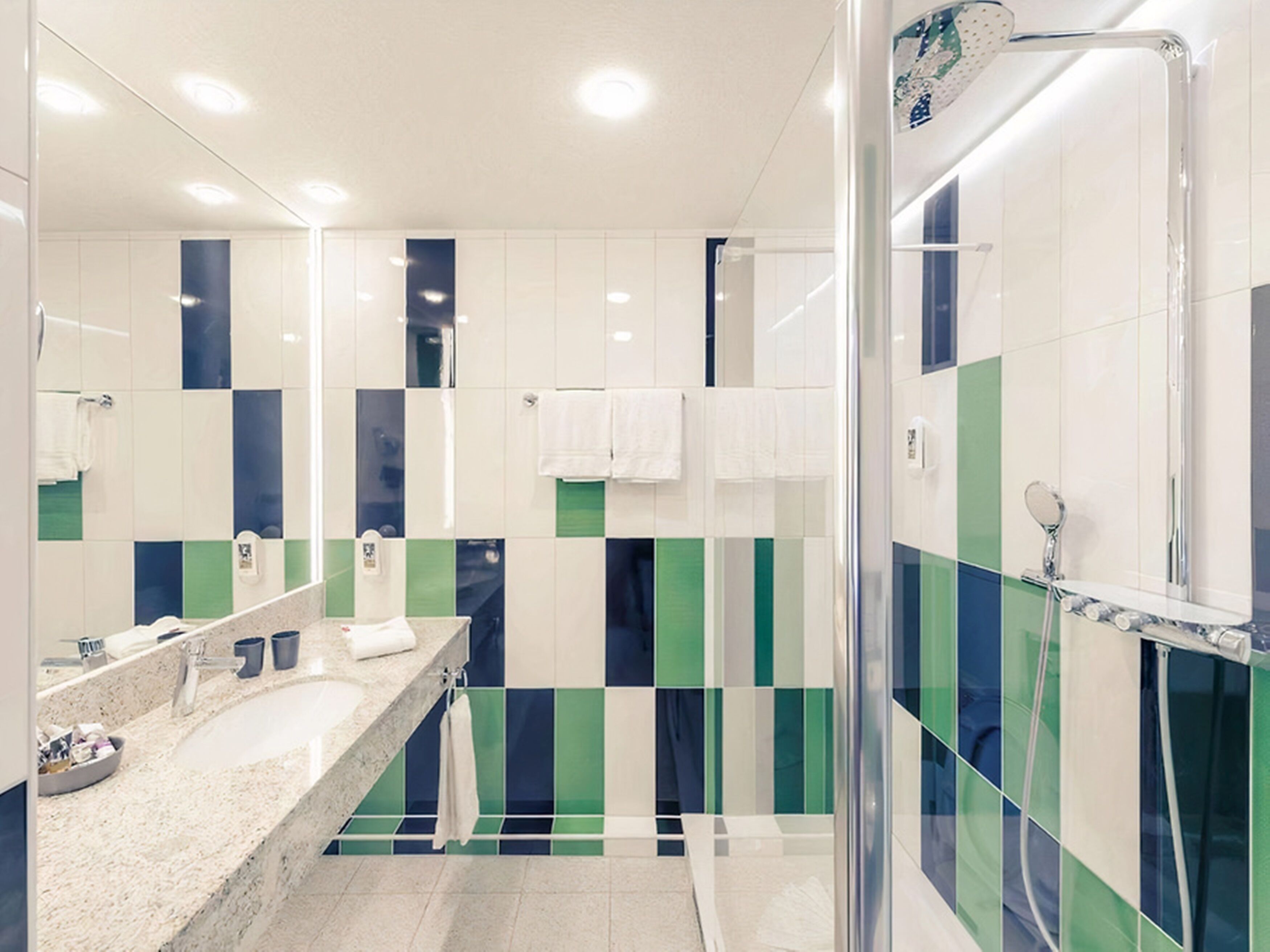 Un baño moderno con un espejo grande, dos lavamanos, una ducha y cabina de ducha con paredes de vidrio.