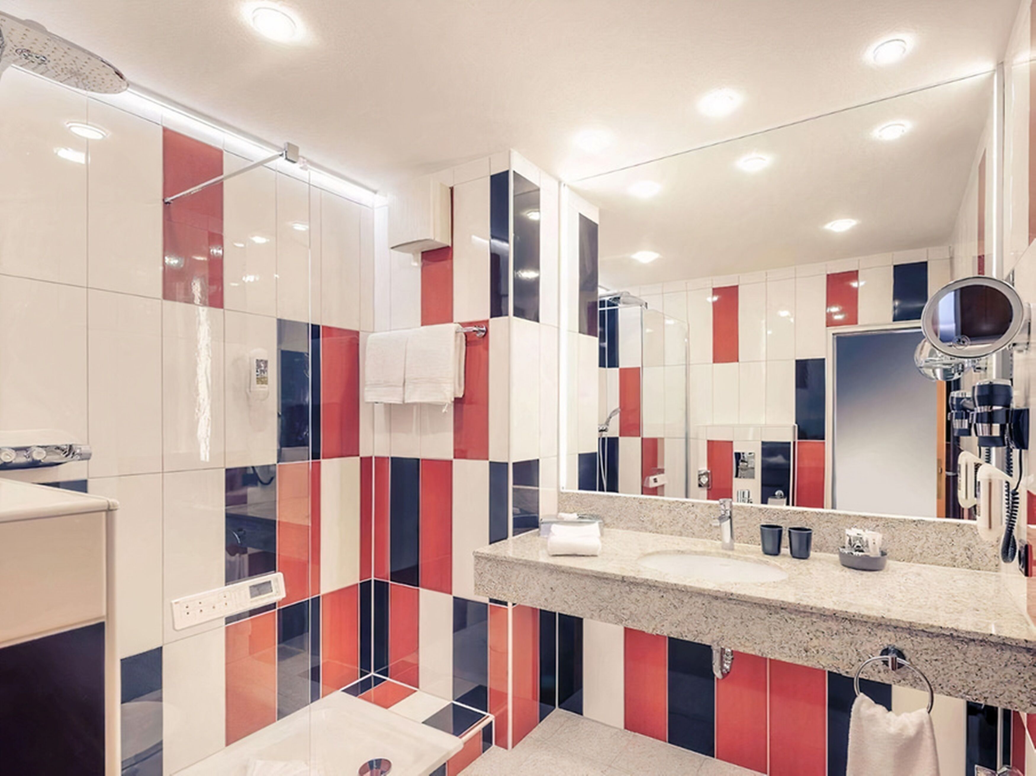 A modern bathroom with a large mirror, a shower, and a vanity with a granite countertop.