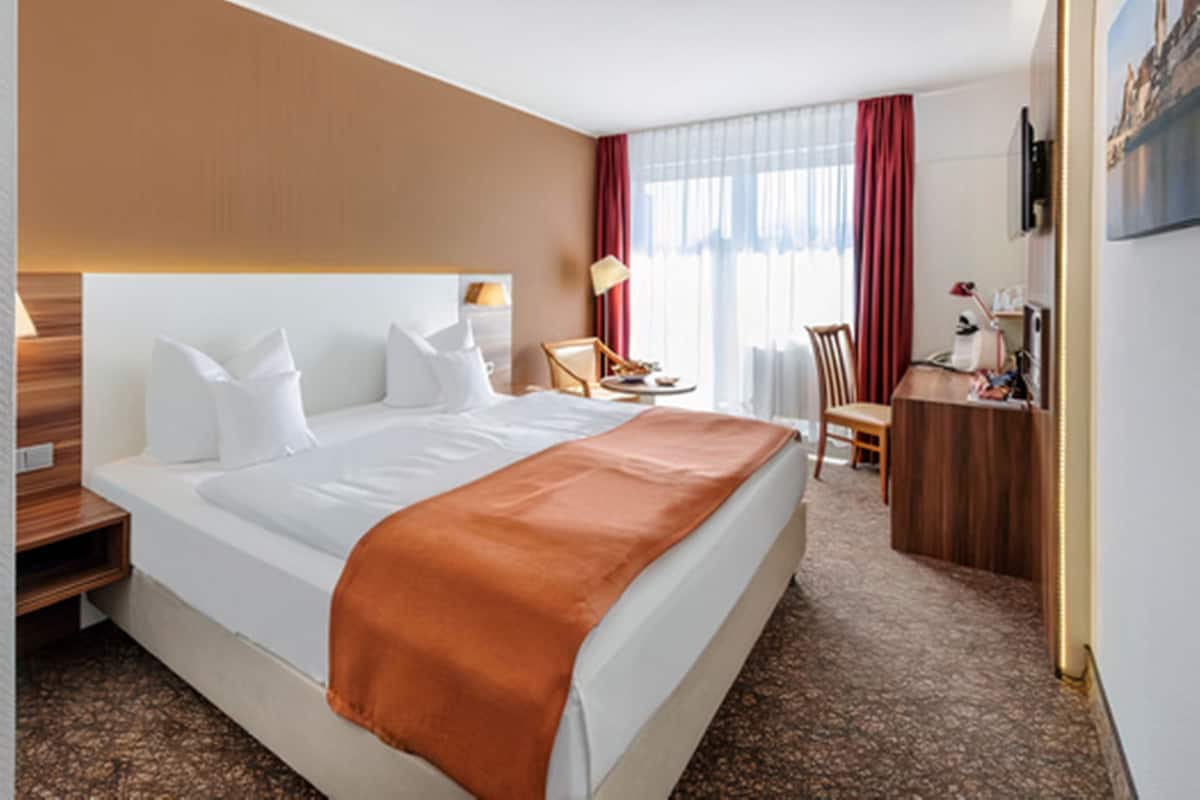 Ein Hotelzimmer mit einem großen Bett, einem Schreibtisch, einem Stuhl und einer Schreibtischlampe.