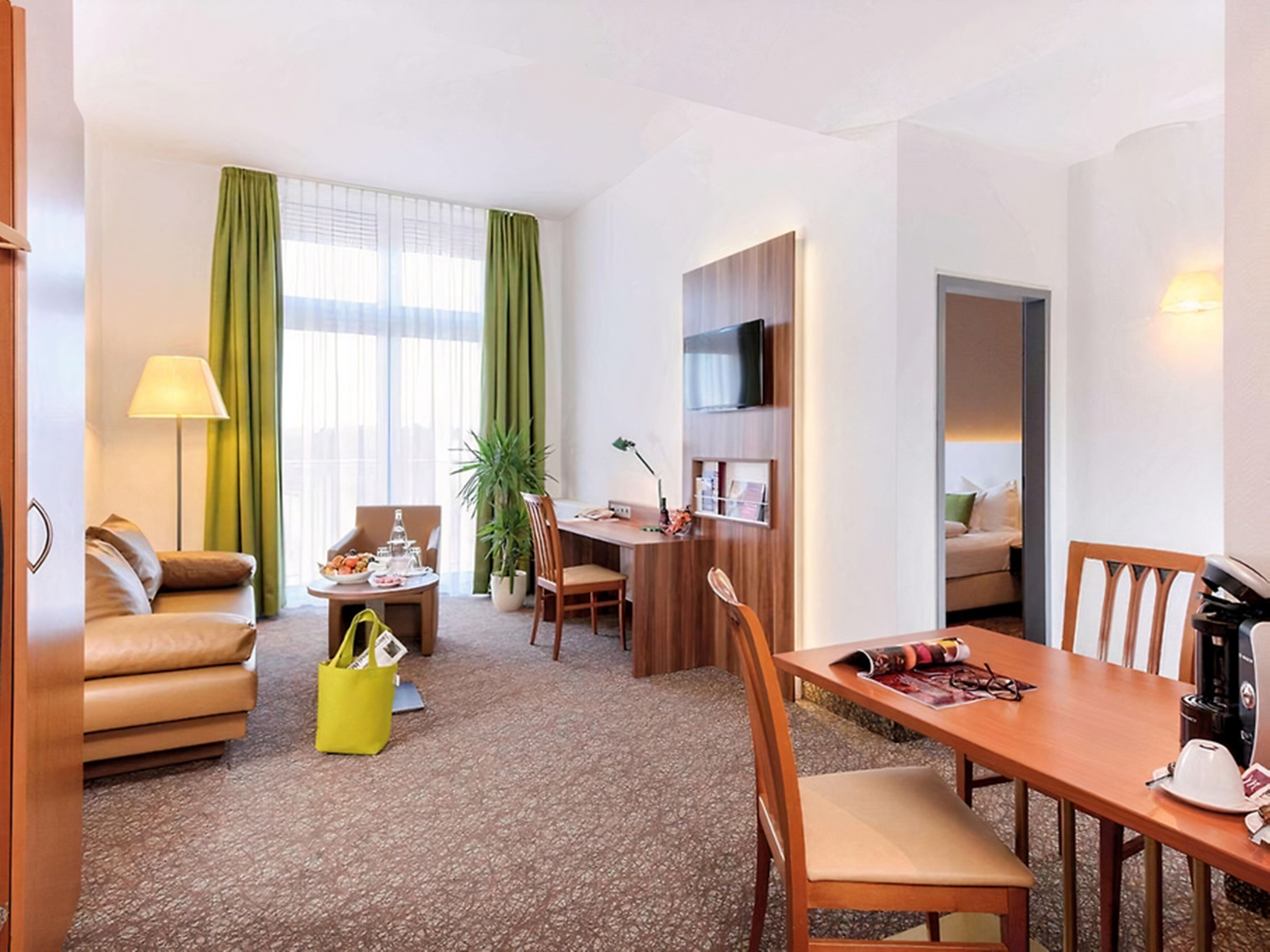 A hotel room with a living area, a dining table, a sofa, a coffee machine, and a TV.