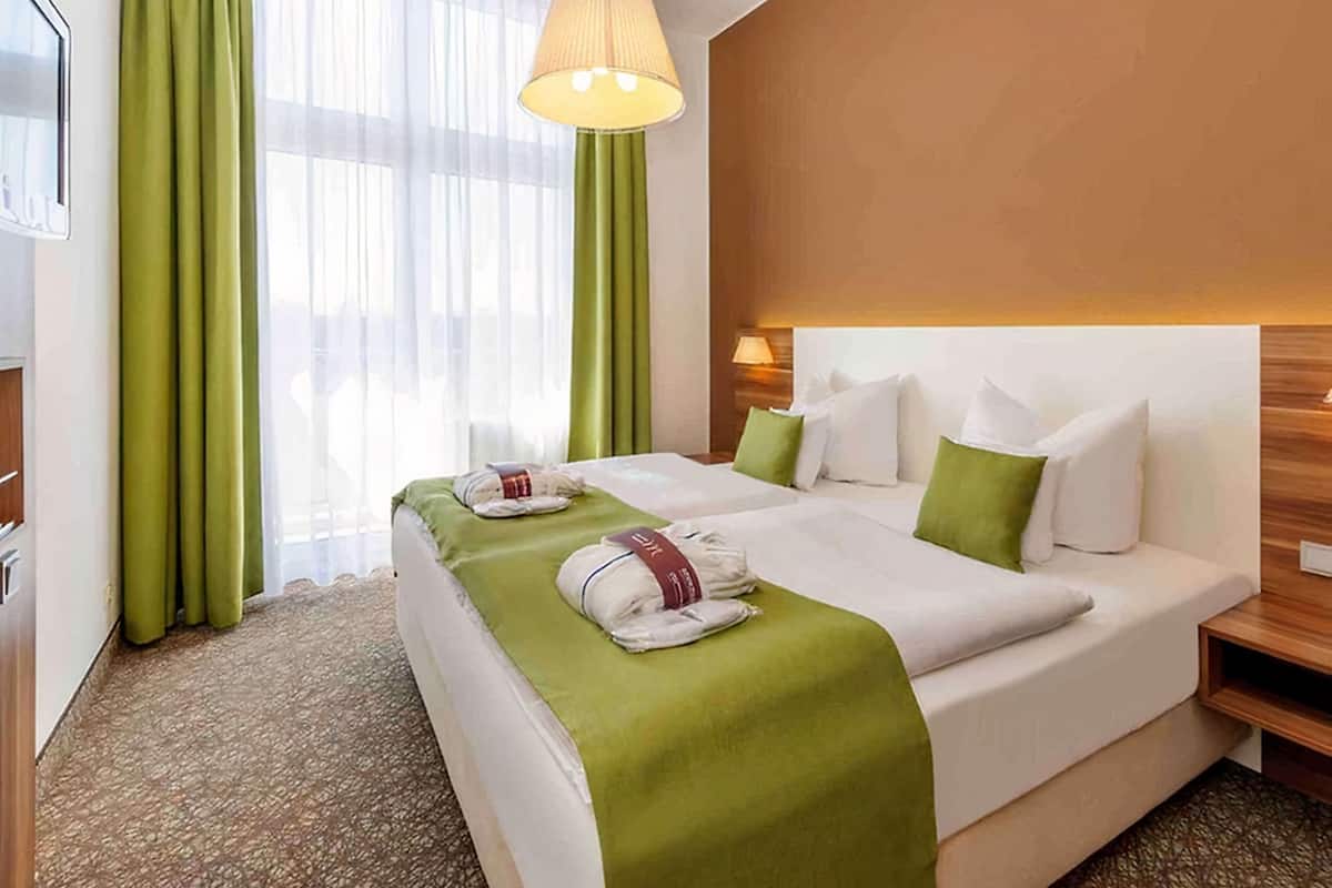 Ein Hotelzimmer mit einem großen Bett, grünen Vorhängen, einer Pendelleuchte und einem hölzernen Kopfteil.