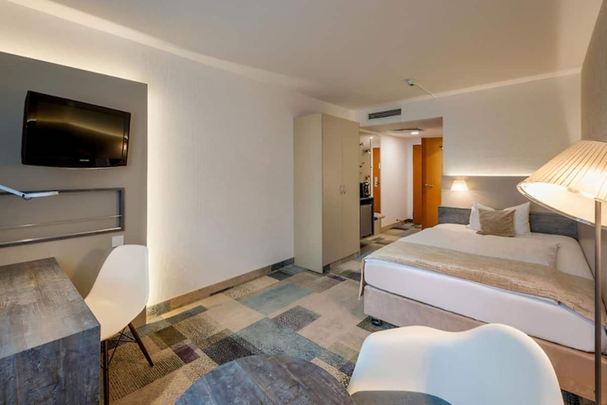 Ein Hotelzimmer mit Bett, Schreibtisch, Stuhl, Wandfernseher und Lampe.