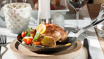 A dining table with a roasted chicken, salad, and wine glasses.