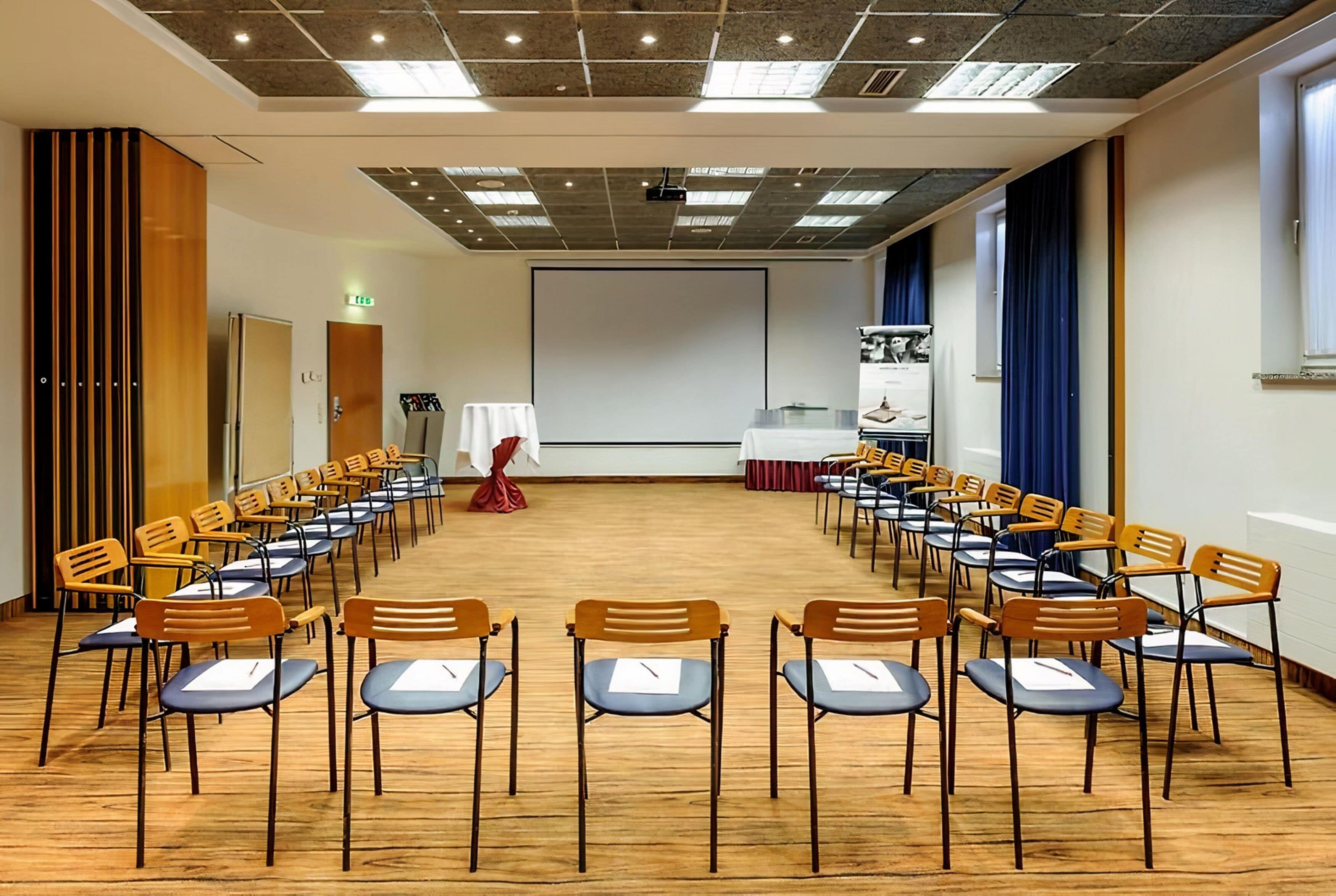 A conference room with rows of chairs, a projector screen, and a presentation area.