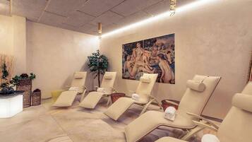 Ein Wellnessraum mit Liegesesseln, einer Massageliege und einem großen Gemälde an der Wand.
