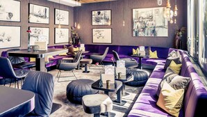 A modern lounge area with purple seating, artwork on the walls, and pendant lighting.