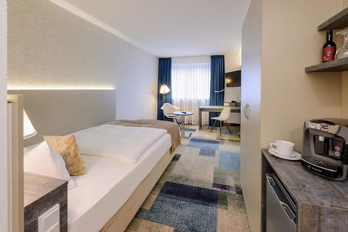 Ein Hotelzimmer mit Bett, Schreibtisch, Stuhl und Küchenzeile.