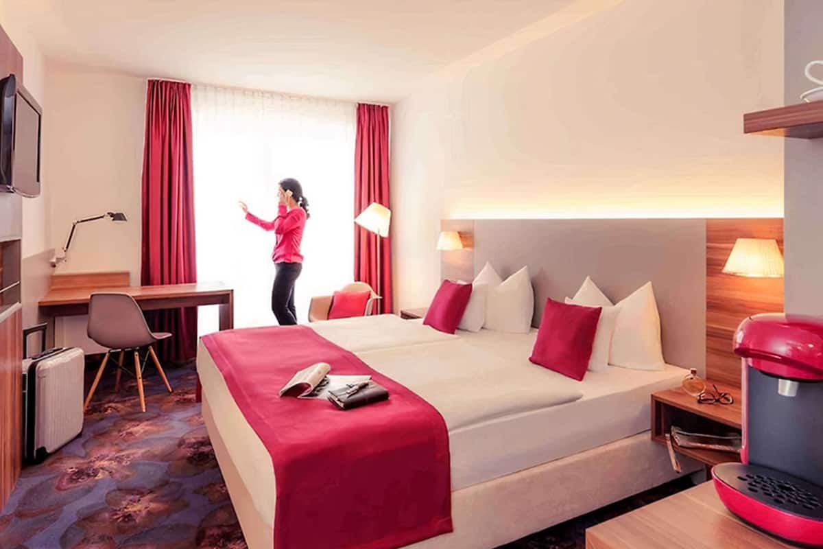 Ein Hotelzimmer mit Bett, Schreibtisch, Stuhl und einem roten Telefon.