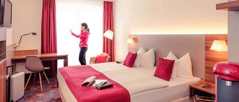 Una habitación de hotel con cama, escritorio, silla y un teléfono rojo.