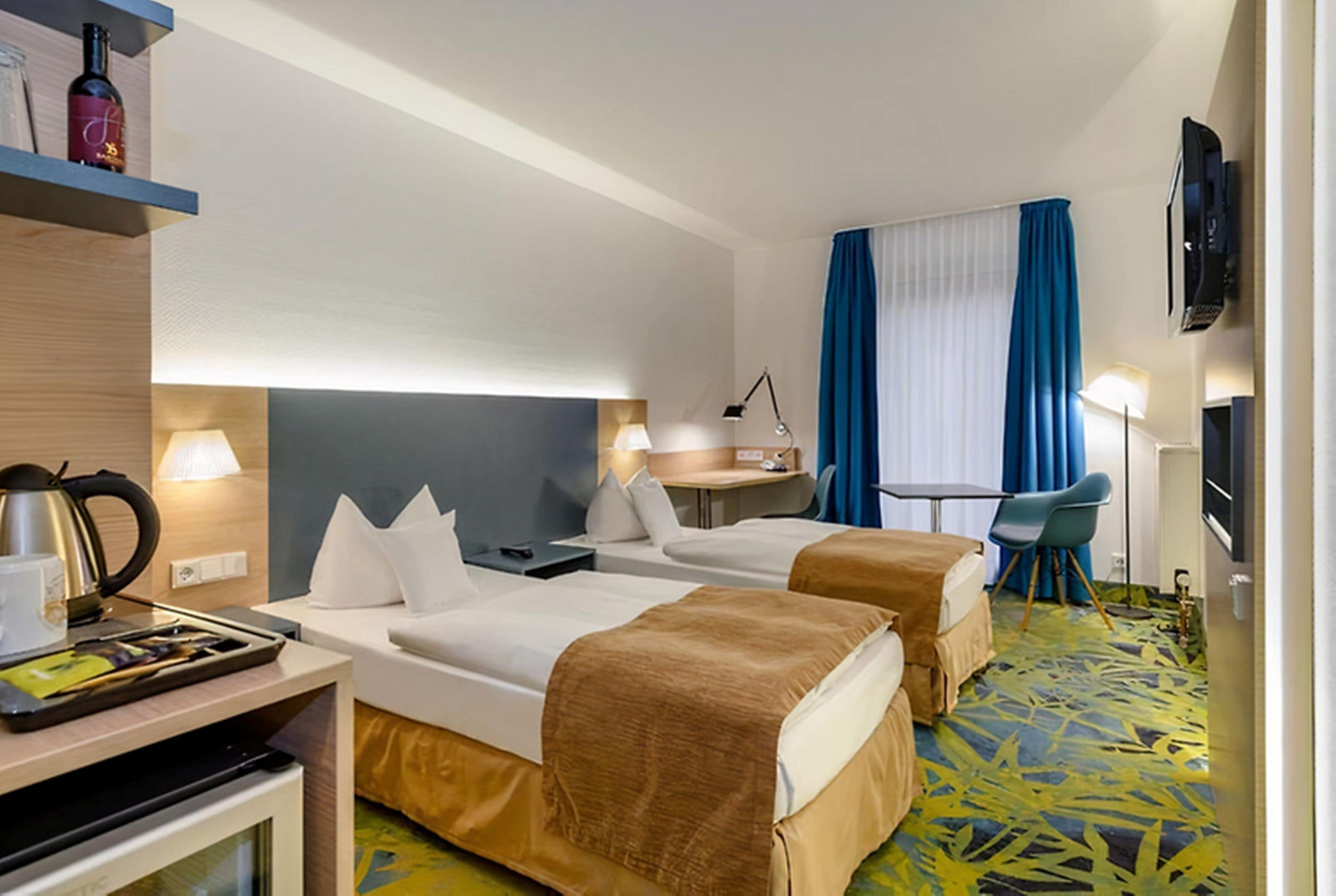 A hotel room with two beds, a desk with a lamp, a television, and a minibar.