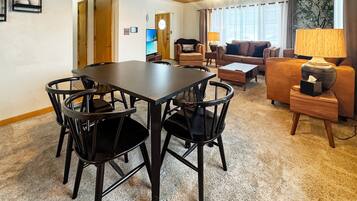 A living room with a dining table, chairs, a sofa, and a lamp.