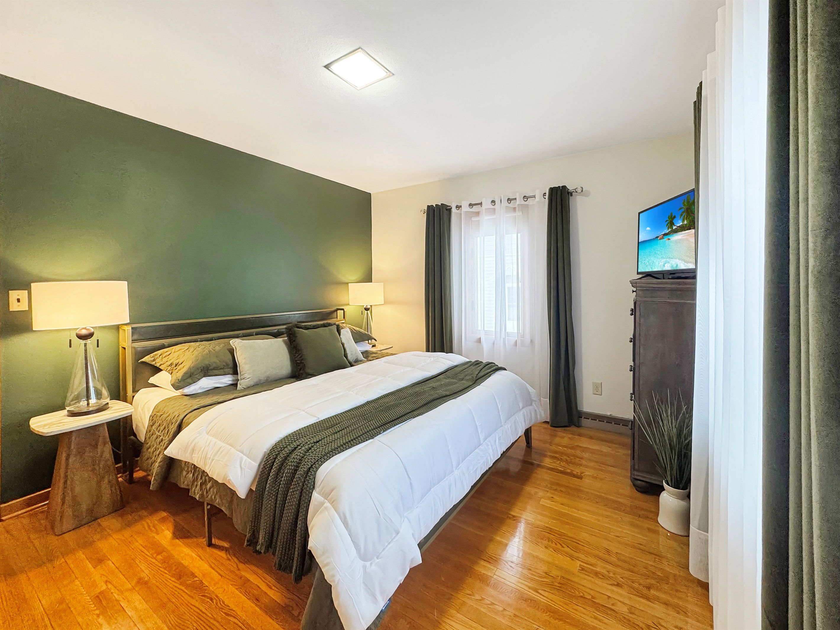 A hotel room with a bed, two bedside lamps, a television on a cabinet, and a window with curtains.