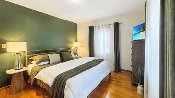 A hotel room with a bed, two bedside lamps, a television on a cabinet, and a window with curtains.