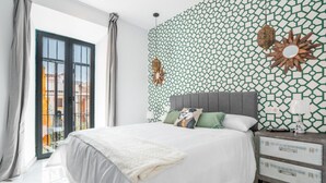 Een moderne slaapkamer met een groot bed, een nachtkastje met lades, een decoratieve wand en uitzicht door een glazen deur.