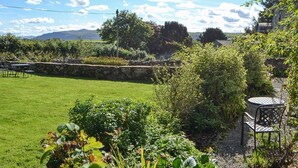 A garden with a stone wall, a grassy lawn, and a metal table and chair. - 3 bedroom accommodation in Sunderland, near Bassenthwaite (Sunderland, near Bassenthwaite)