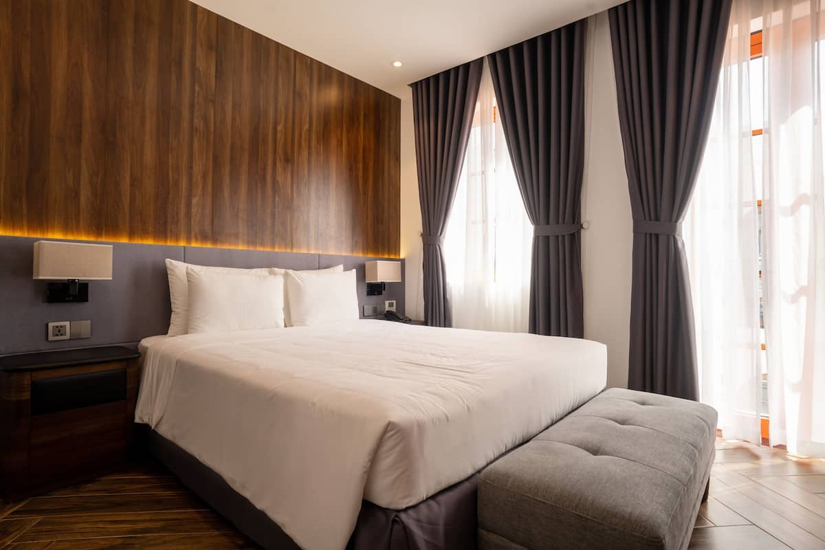 A modern hotel room with a large bed, a bench, and a wooden accent wall.