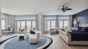 A spacious bedroom with a large bed, a seating area with a chair and a small table, and a balcony with a view of the sea. - 7 Singleton Beach, Oceanfront, Private Pool (Hilton Head Island)