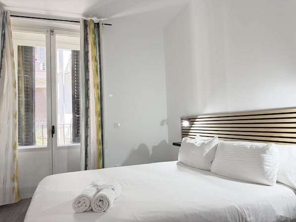 Ein Hotelzimmer mit Bett, einem Fenster mit Vorhängen und Blick ins Freie.
