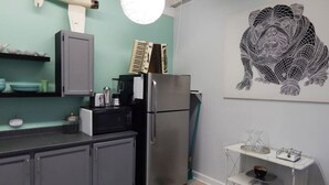 Een keuken met grijze kastjes, een roestvrijstalen koelkast, een klein eiland met een spoelbak en een wandlamp.
