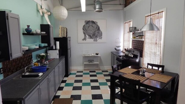 Een kleine keuken met een zwart-wit geruite vloer, een eettafel met stoelen en een groot kunstwerk aan de muur.