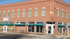 A red brick building with multiple storefronts, a green awning, and a sign indicating a business.