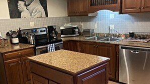 A kitchen with wooden cabinets, a granite countertop island, stainless steel appliances, and a tiled backsplash.