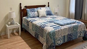A bedroom with a wooden bed, a nightstand with a lamp, a painting on the wall, and a window with curtains.