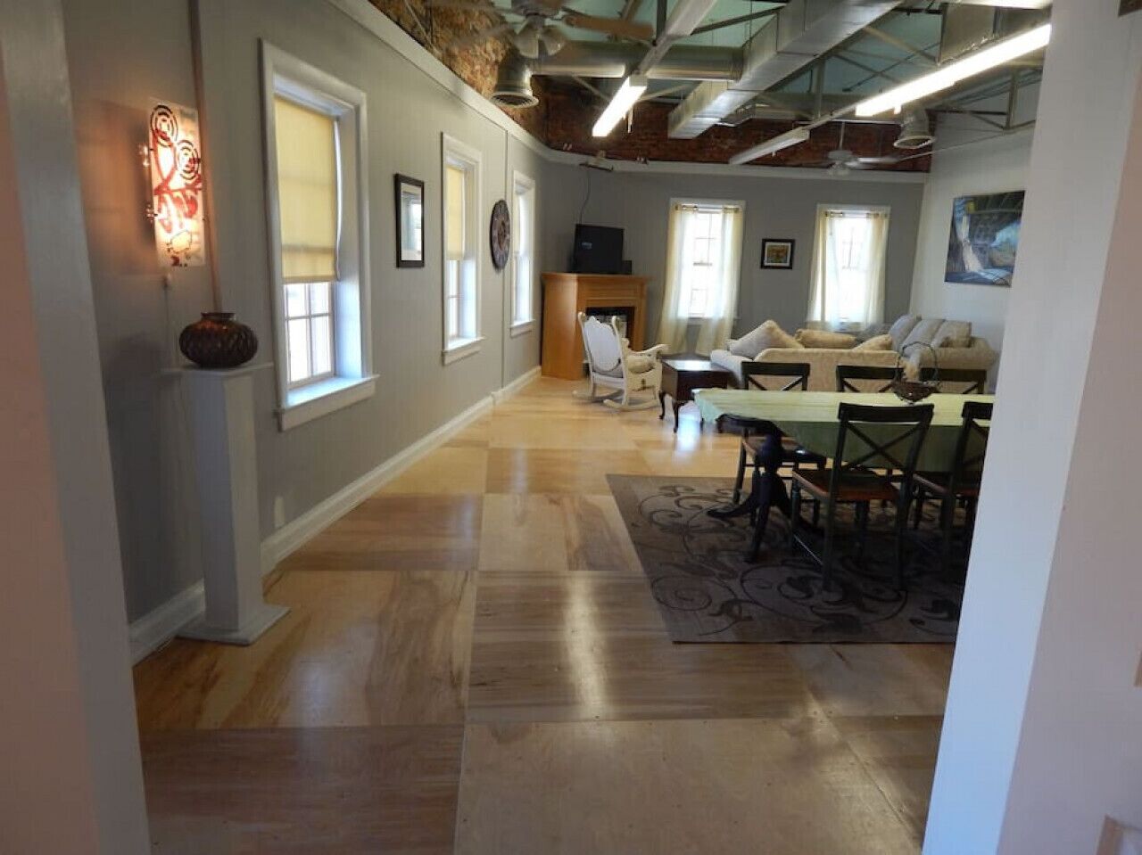 A spacious living area with hardwood flooring, a fireplace, a dining table with chairs, and a large window providing natural light.