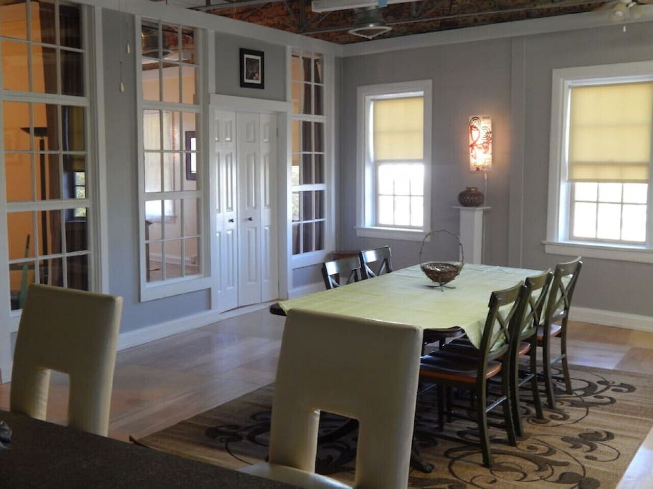 Un comedor con una mesa dispuesta para seis personas, rodeada de sillas, en una habitación con ventanas amplias y vistas al exterior.