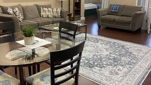 A living room with a glass coffee table, two sofas, a rug, a painting, and a bookshelf.