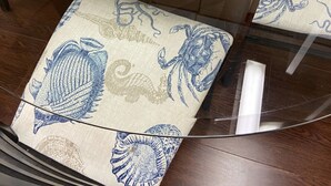 A round glass table with a potted plant, a coaster with a crab design, and matching upholstered chairs with a blue sea creature pattern.
