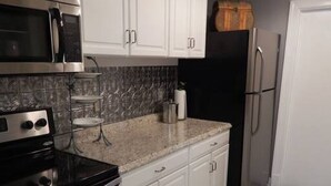 A kitchen with white cabinets, a black stove, a microwave, a refrigerator, and a checkered floor.