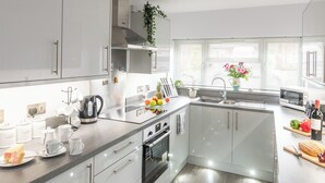 A modern kitchen with white cabinets, a stainless steel range, and a built-in oven. - 3 bedroom accommodation in Sheringham (Sheringham)