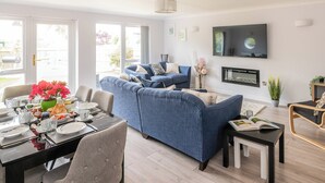 A modern living room with a blue sofa, dining table set, and a flat-screen TV mounted on the wall. - 3 bedroom accommodation in Sheringham (Sheringham)