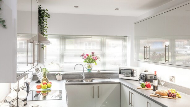 A modern kitchen with a built-in microwave, sink, and stainless steel appliances. There is a window with blinds, a plant on the windowsill, and a variety of fruits and vegetables on the counter. - 3 bedroom accommodation in Sheringham (Sheringham)