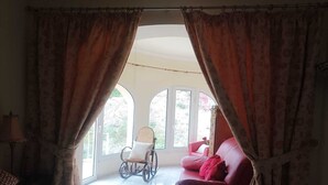A bedroom with a bed, a rocking chair, a red sofa, and a large window with curtains. - "La Favorita: Mountain Serenity with Ocean Views". (Calpe)