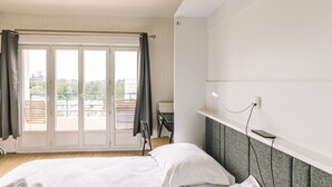Hotellihuone, jossa on sänky, työpöytä ja liukuovesta avautuva näkymä ulos.