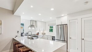 A modern kitchen with white cabinetry, a large island with bar stools, stainless steel appliances, and recessed ceiling lighting.