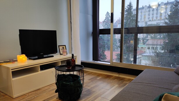 Uma sala de estar moderna, com uma janela ampla, uma TV de tela plana, uma mesinha e um sofá aconchegante.