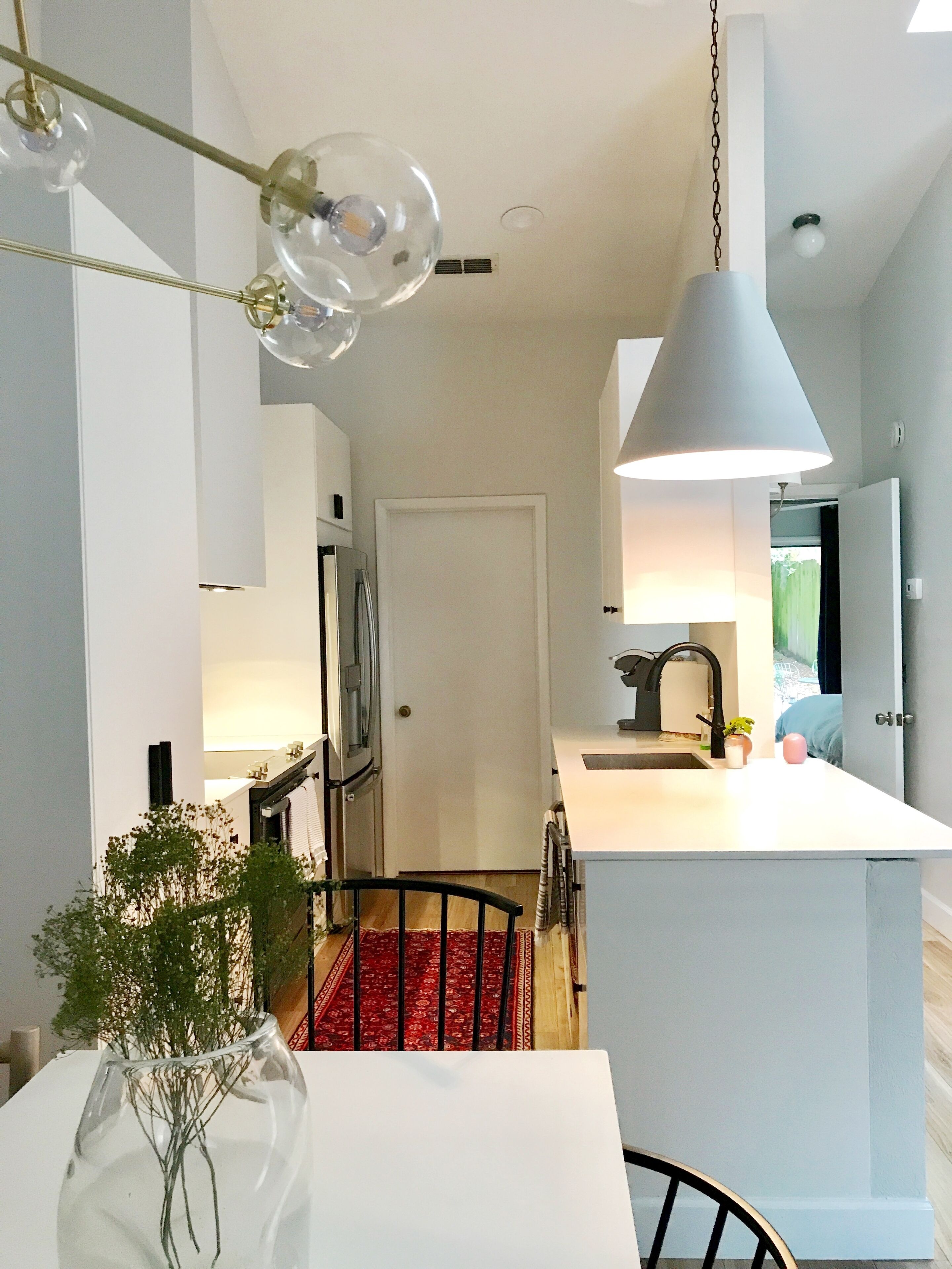 A modern kitchen with a central island, a dining area with a red rug, and a clear vase with greenery.
