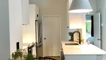 A modern kitchen with a central island, a dining area with a red rug, and a clear vase with greenery.