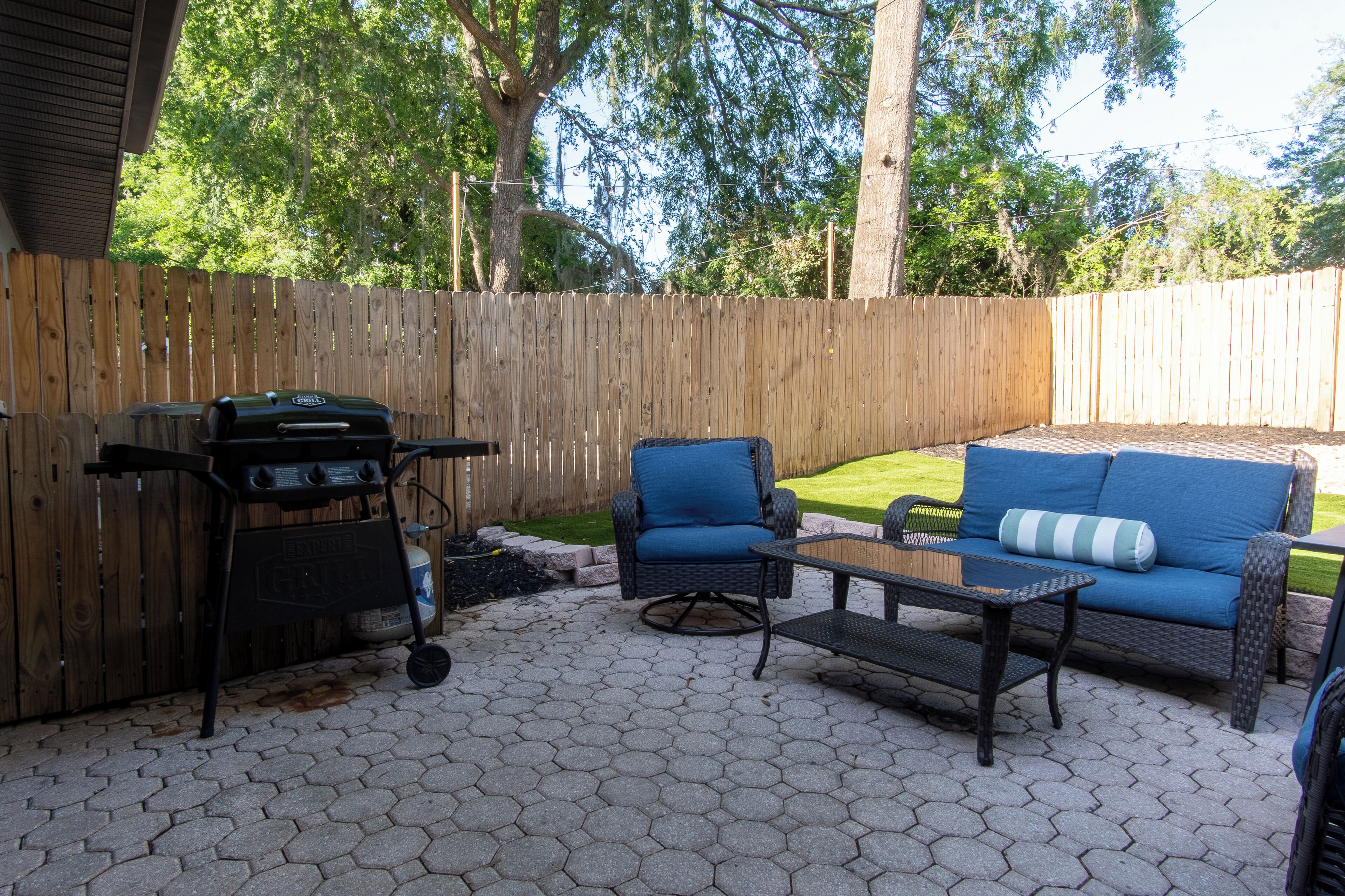 An outdoor patio with a grill, a blue cushioned chair, and a sofa with a striped pillow.