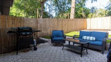An outdoor patio with a grill, a blue cushioned chair, and a sofa with a striped pillow.