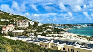 A coastal town with buildings, solar panels on rooftops, and a beach in the background.