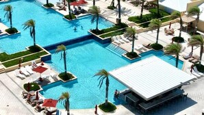 A large outdoor swimming pool with multiple sections, surrounded by palm trees and sun loungers.