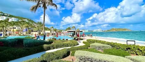 A resort with a swimming pool, palm trees, and a beach.